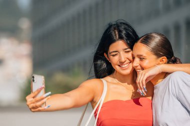 Kızlar sokakta cep telefonu kaydıyla eğleniyorlar ya da selfie çekiyorlar.