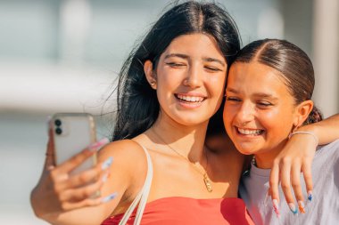 Kızlar sokakta cep telefonu kaydıyla eğleniyorlar ya da selfie çekiyorlar.