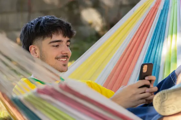 带着手机坐在吊床上的年轻男性 图库图片
