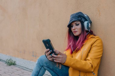 Kulaklık ve cep telefonuyla sokakta oturan şehirli kız.