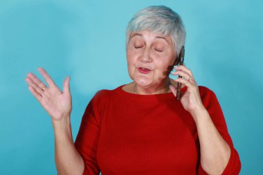 60 'lı yaşlarda yalnız bir kadın cep telefonuyla konuşuyor.