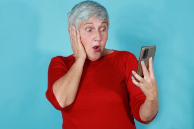 İzole edilmiş 60 'lı yaşlarda bir kadın telefonuna şaşkın bir ifadeyle bakıyor.