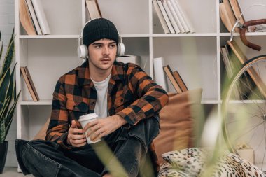 Evde kulaklığı ve cep telefonu olan genç bir adam.