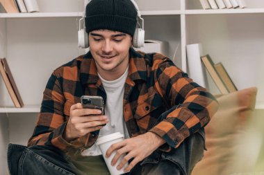 Evde kulaklığı ve cep telefonu olan genç bir adam.
