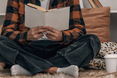 Genç adam sonbahar kış kıyafetleri içinde kitap okuyor.