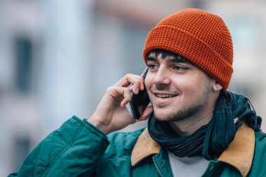 Genç adam kışın sokakta cep telefonuyla konuşuyor.