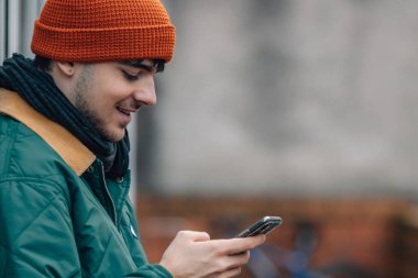 Şapkalı ve kalın elbiseli genç bir adamın portresi cep telefonuna bakıyor.