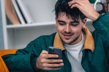 Evdeki genç adam cep telefonuna bakıyor.