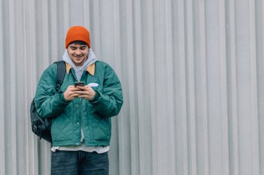 Arka planda cep telefonu olan genç adam kışlık giysiler giyiyor.