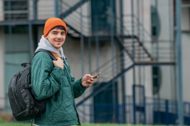 Sırt çantalı genç bir adam ya da öğrenci cep telefonuna bakıyor.