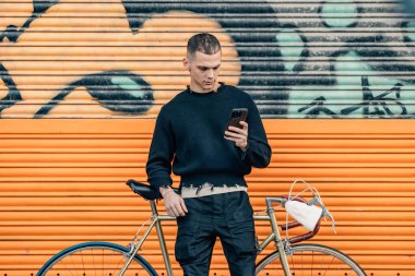 Şehir arka planında cep telefonu ve bisikleti olan şık bir genç adam.