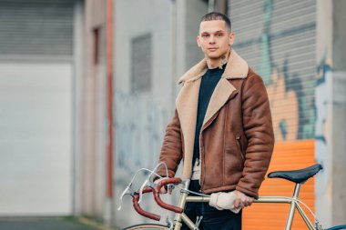 Şehir arka planında bisikleti olan şık bir genç adam.