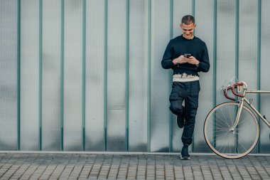 Sokak duvarı arka planı ve kopyalama alanı olan bisiklet ve cep telefonlu genç adam