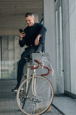 Bisikletli genç adam cep telefonuna bakıyor.