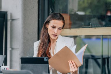 Terasta dizüstü bilgisayarı olan iş kadını belgeleri inceliyor.