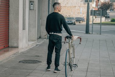 Sırtında bisikletle sokakta yürüyen genç adam.