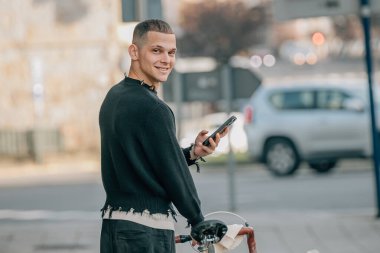 Bisiklet ve cep telefonuyla sokakta yürüyen genç adam.