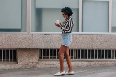 Cep telefonu ve fincanla yürüyen kadın.