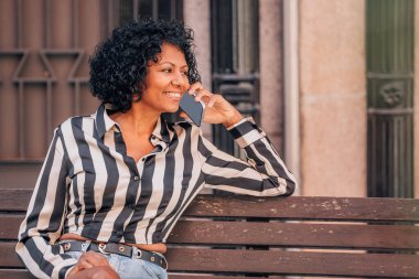 Sokakta oturan mutlu kadın cep telefonuyla konuşuyor.