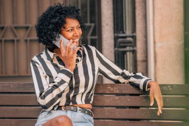 Sokakta oturan mutlu kadın cep telefonuyla konuşuyor.