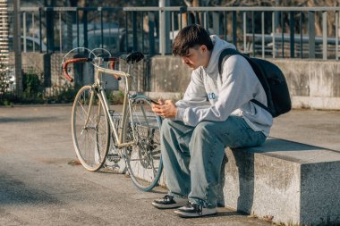 Sokakta oturan genç adam cep telefonu ve bisikletiyle