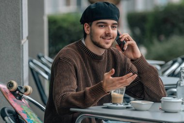 Kafe terasında cep telefonu ve kaykaylı genç bir adam.