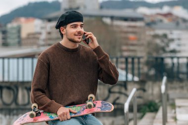 Sokaktaki genç adam cep telefonu ve kaykayıyla