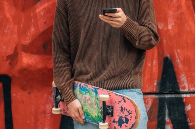 Sokaktaki genç adam cep telefonu ve kaykayıyla