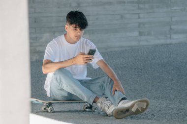 Öğrenci ya da sokakta cep telefonu ve kaykayı olan genç bir adam.