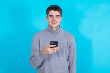 Mavi arka planda cep telefonu ya da akıllı telefonu olan gülümseyen genç adam izole edildi