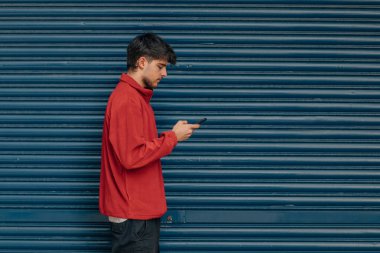 Genç adam sokakta yürürken cep telefonuna ya da akıllı telefona bakıyor.