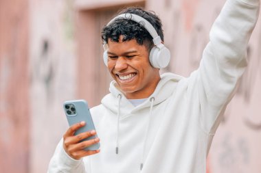 Kulaklıklı genç Latin adam dışarıda mutlu mesut eğleniyor.