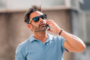 Güneş gözlüklü çekici bir genç yazın sokakta cep telefonuyla konuşuyor.