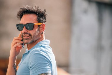 Güneş gözlüklü çekici bir genç yazın sokakta cep telefonuyla konuşuyor.