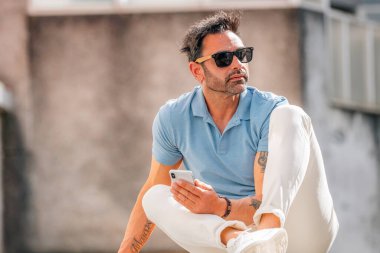 Yazın sokakta güneş gözlüklü ve cep telefonlu çekici Latin bir adam.