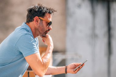 Güneş gözlüklü çekici bir genç adam sokakta cep telefonuna bakıyor.