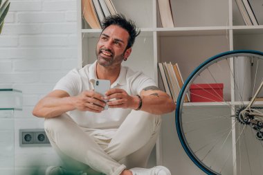 Evde cep telefonu yerde oturan çekici bir adam.