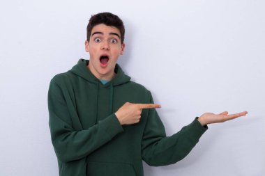 Afallamış genç beyaz arka planı işaret ediyor.