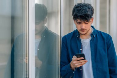 Genç bir adam ya da çocuk sokakta cep telefonuna bakıyor.