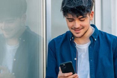 Genç bir adam ya da çocuk sokakta cep telefonuna bakıyor.