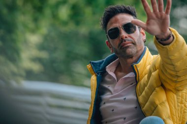 Sokak ortasında güneş gözlüklü İspanyol adam el sallıyor.