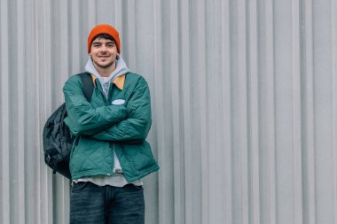 Sırt çantası ve kalın giysileri olan genç adam sokak duvarında.