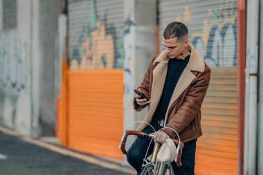 Şehir arka planında cep telefonu ve bisikleti olan şık bir genç adam.