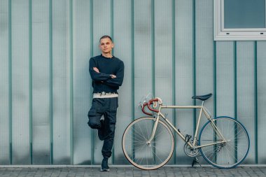 Sokak duvarı arka planı ve kopyalama alanı olan bisikletli genç bir adam.