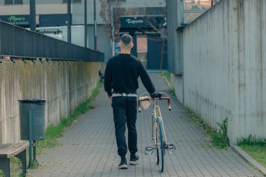 Bisikletli genç adam sokakta yürüyor.