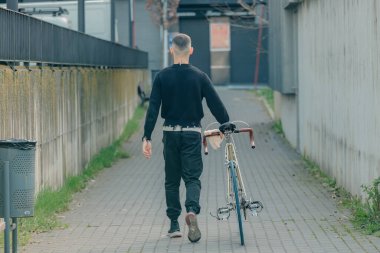 Bisikletli genç adam sokakta yürüyor.