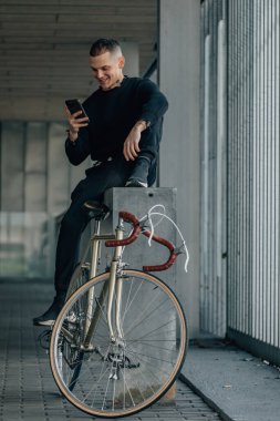 Bisikletli genç adam cep telefonuna bakıyor.