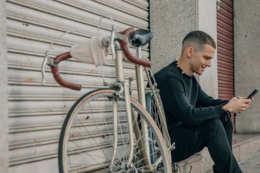 Genç adam cep telefonuyla sokakta oturuyor.