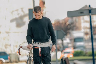 Genç adam bisikletle sokakta yürüyor.