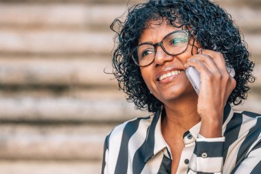 Latin Afrikalı Amerikalı kadın sokakta cep telefonuyla oturuyor.